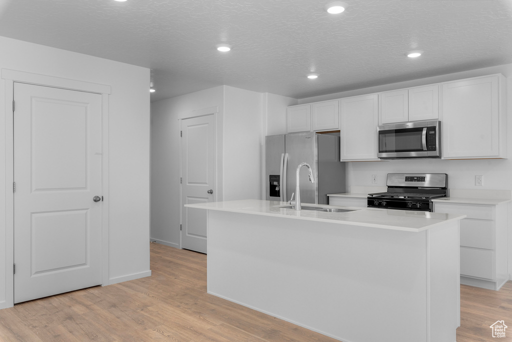 Kitchen with stainless steel appliances, white cabinetry, a kitchen island with sink, light countertops, and recessed lighting