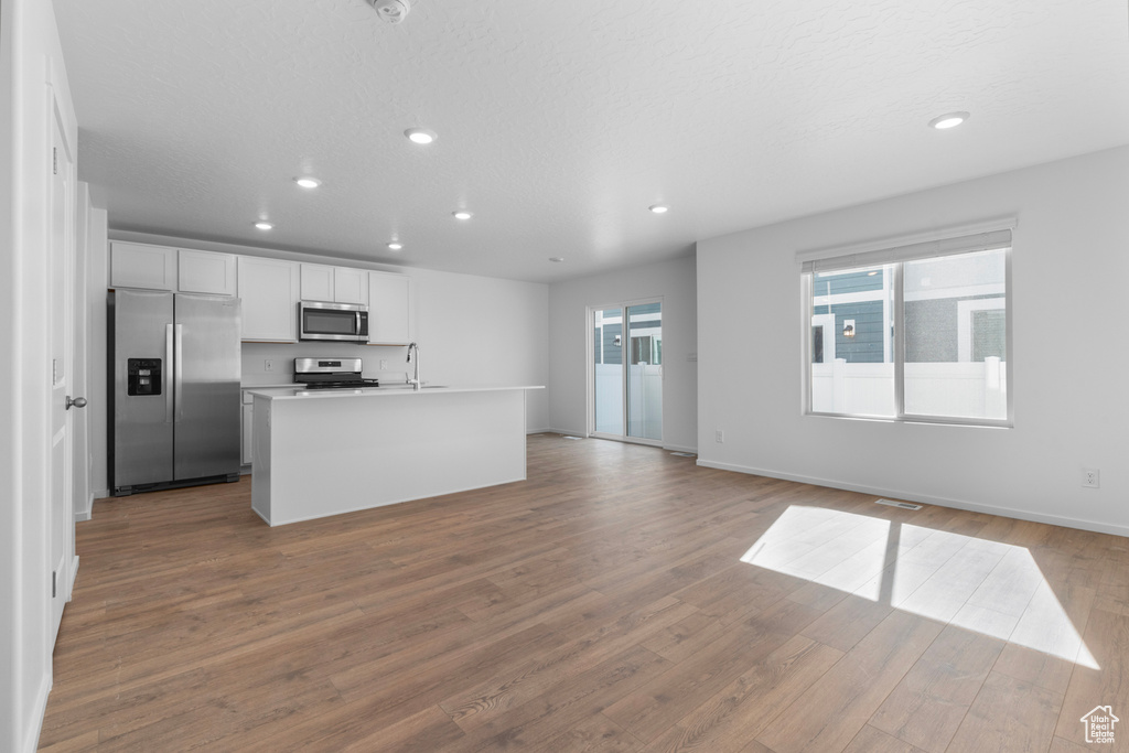 Kitchen featuring appliances with stainless steel finishes, recessed lighting, white cabinetry, open floor plan, and wood finished floors