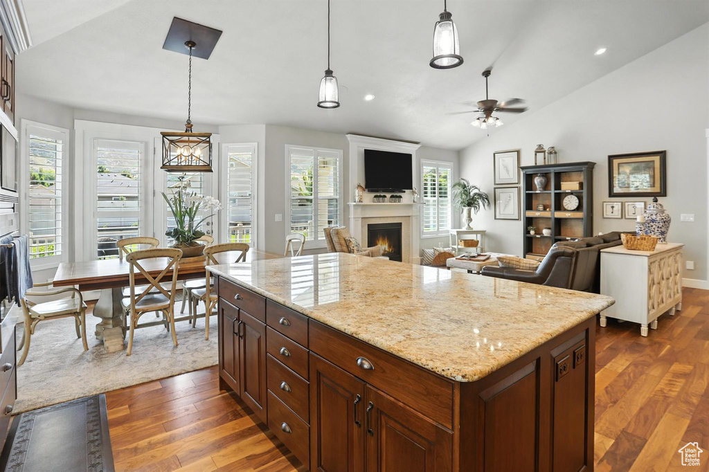 Kitchen with vaulted ceiling, a warm lit fireplace, dark wood-style floors, ceiling fan, and hanging light fixtures