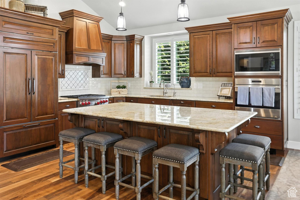 Kitchen with built in appliances, custom range hood, lofted ceiling, backsplash, and wood finished floors