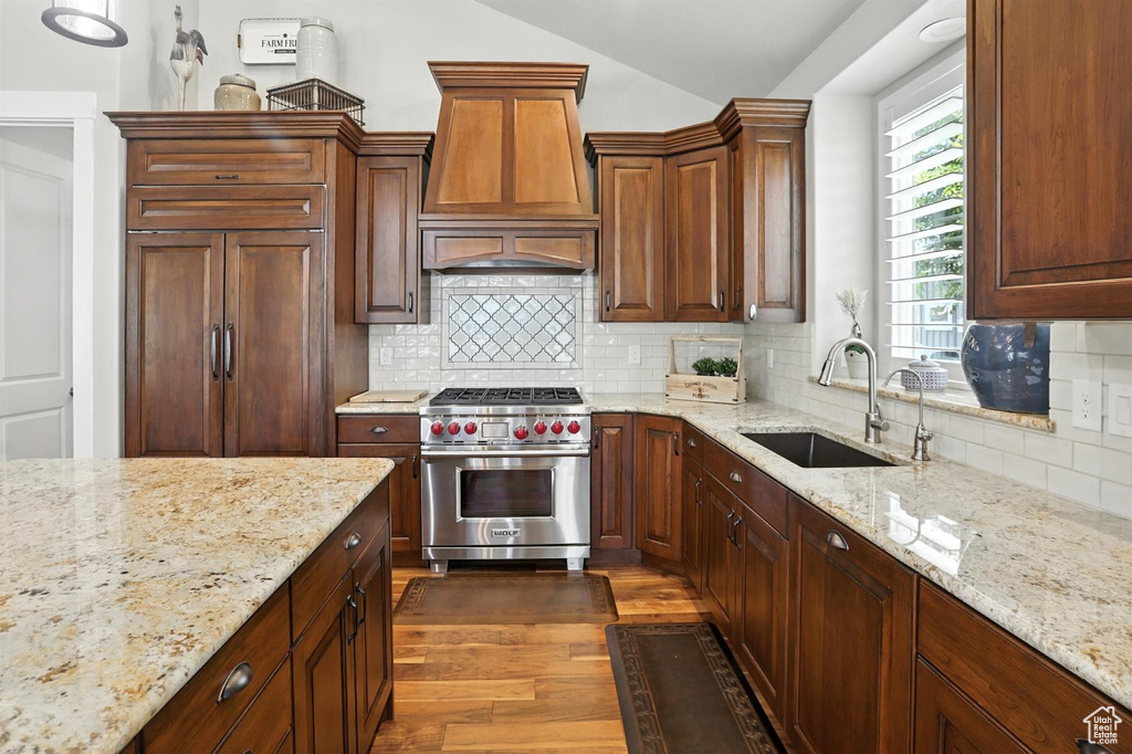 Kitchen with high end appliances, custom exhaust hood, vaulted ceiling, dark wood-style floors, and backsplash