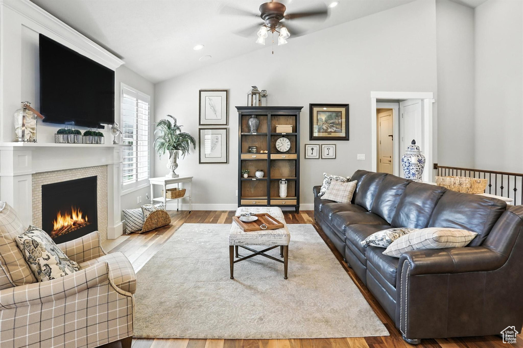 Living room with vaulted ceiling, ceiling fan, wood finished floors, and a warm lit fireplace