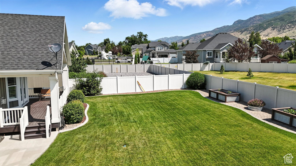 Fenced backyard with a residential view, a deck with mountain view, and a vegetable garden