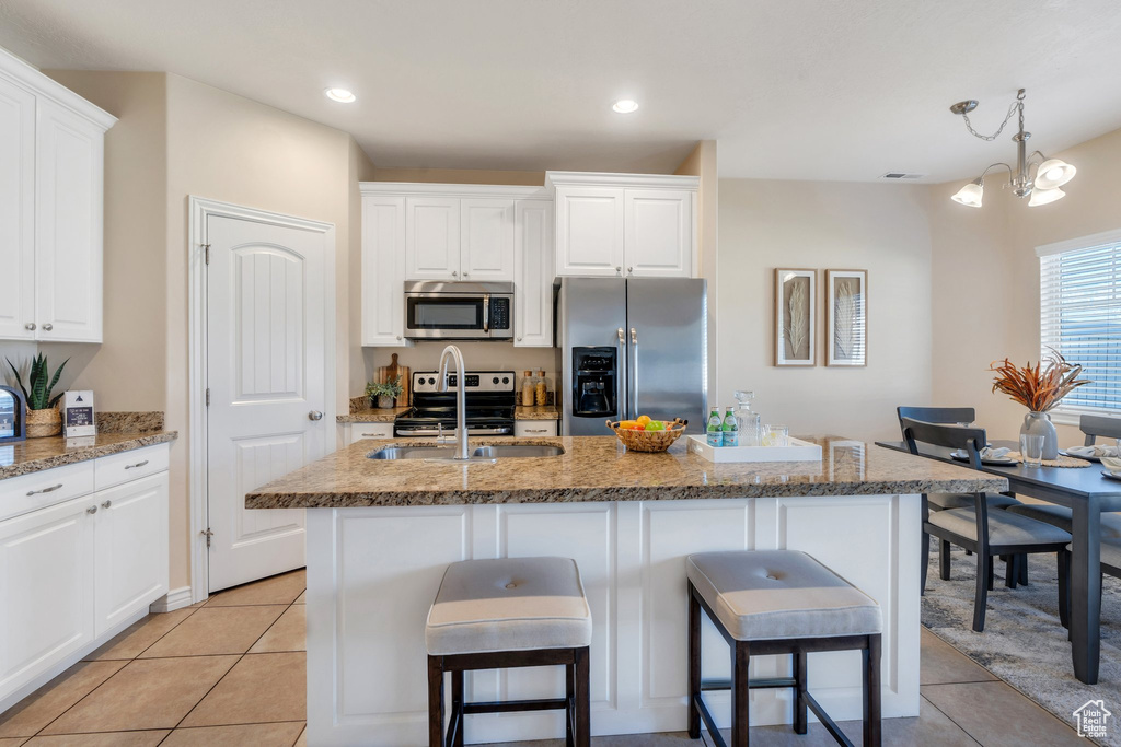 Kitchen featuring stainless steel appliances, a breakfast bar area, a center island with sink, light tile patterned floors, and recessed lighting