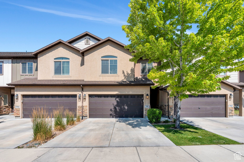 View of front of house with stone siding, a garage, driveway, and stucco siding