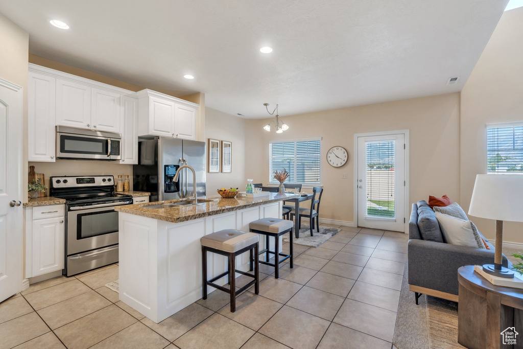 Kitchen featuring appliances with stainless steel finishes, a kitchen bar, light tile patterned floors, stone counters, and recessed lighting
