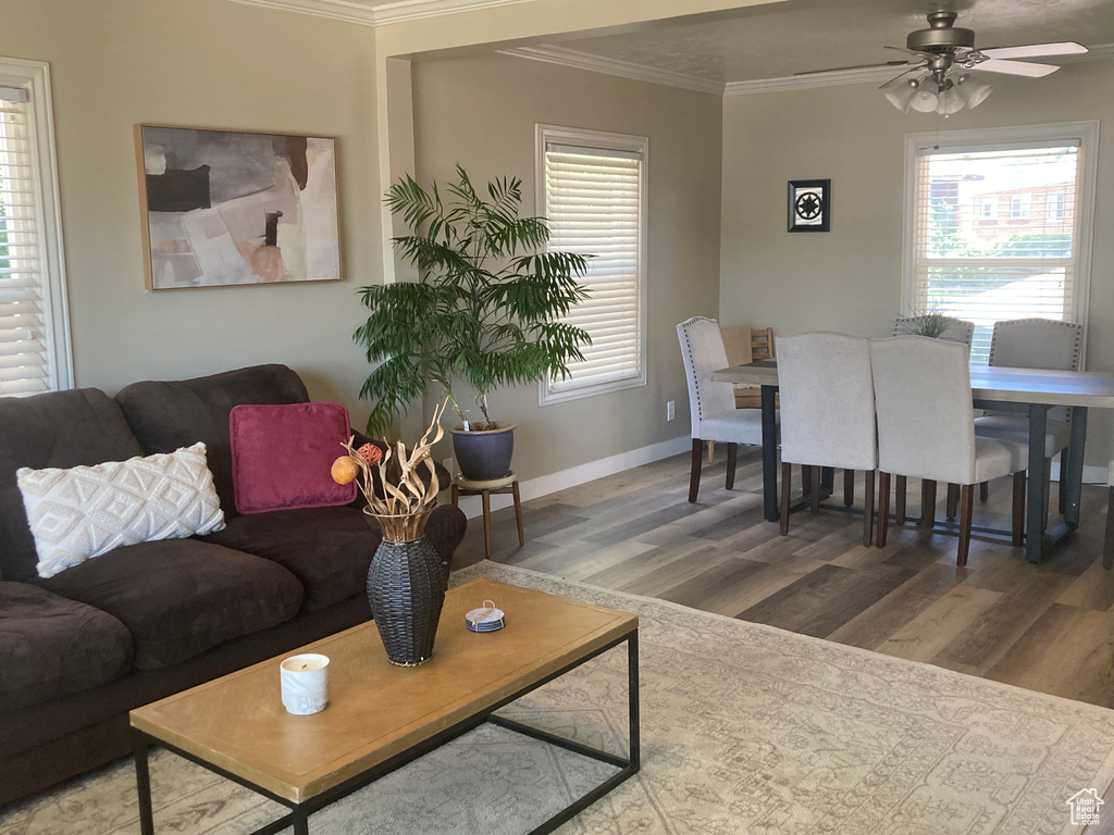 Living area with wood finished floors, ornamental molding, a ceiling fan, and healthy amount of natural light