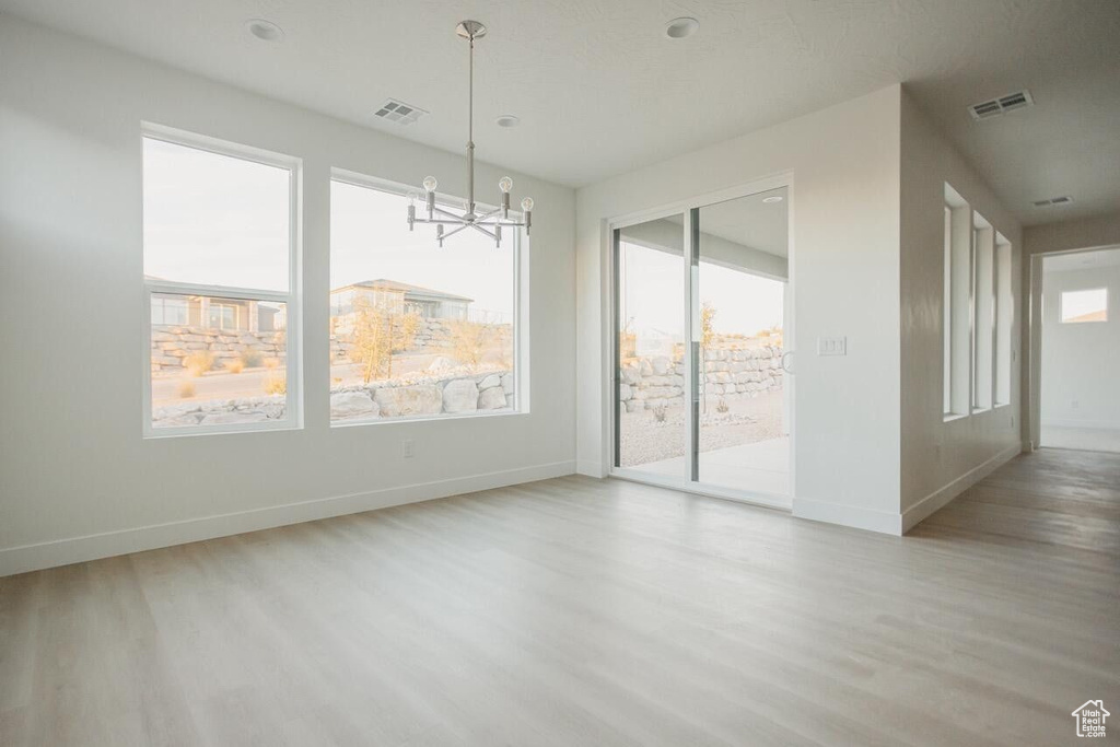 Unfurnished room featuring wood finished floors, plenty of natural light, and a chandelier