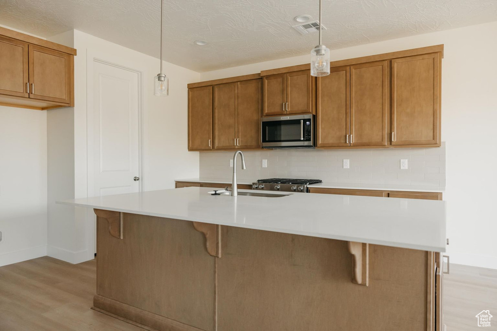 Kitchen featuring stainless steel microwave, light wood-type flooring, brown cabinetry, pendant lighting, and light countertops