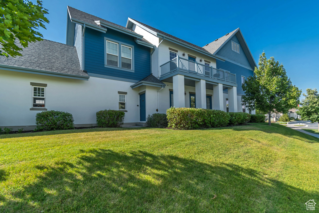 View of front of property with a balcony, a front lawn, a shingled roof, and stucco siding