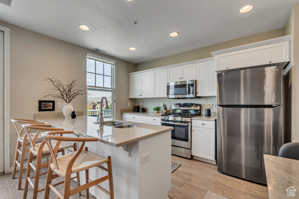 Kitchen featuring appliances with stainless steel finishes, recessed lighting, a kitchen bar, white cabinetry, and light countertops
