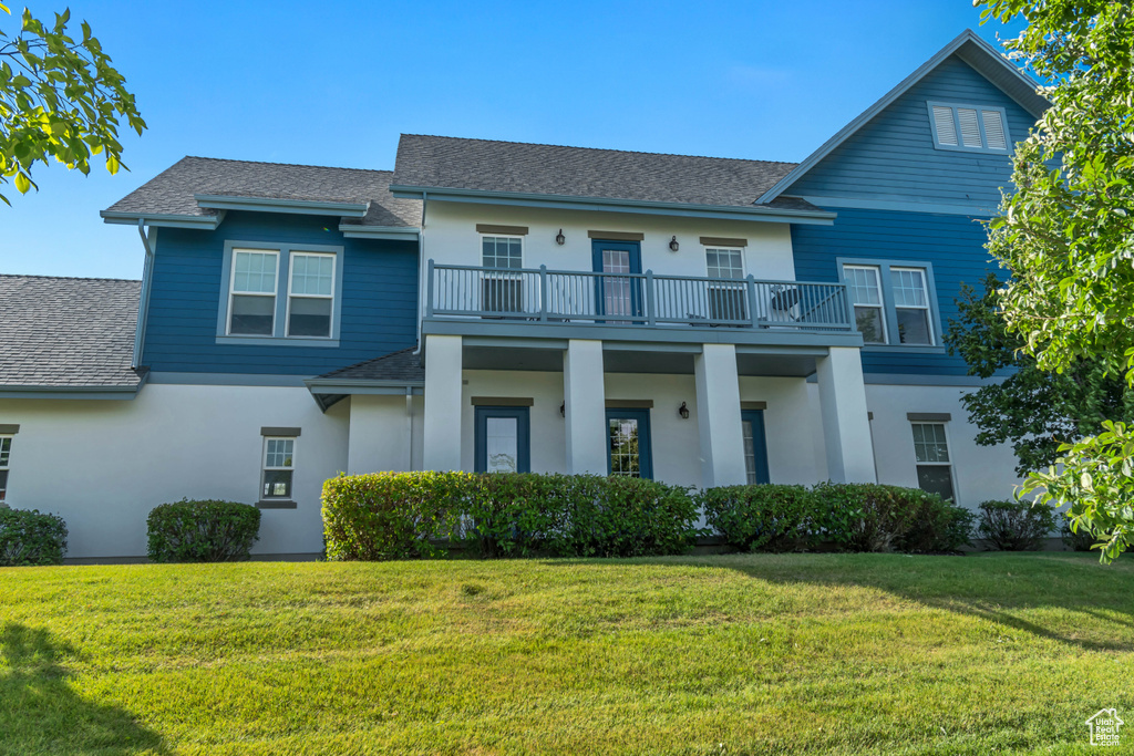View of front of property with stucco siding, roof with shingles, a front lawn, and a balcony