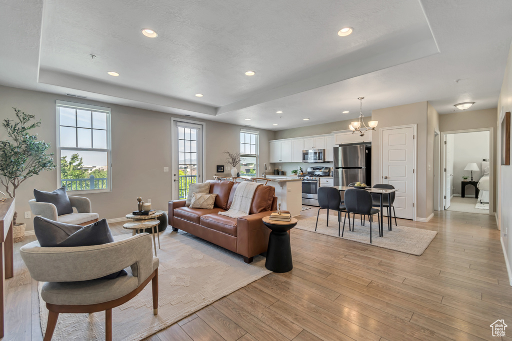 Living room featuring a tray ceiling, a chandelier, light wood-style floors, and recessed lighting