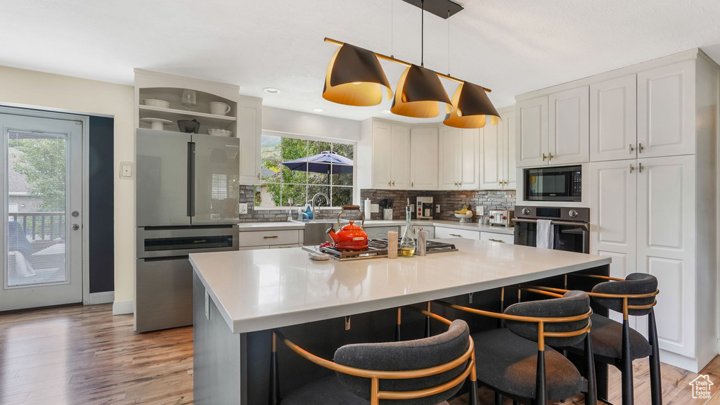 Kitchen with appliances with stainless steel finishes, decorative backsplash, light wood finished floors, a kitchen breakfast bar, and a kitchen island