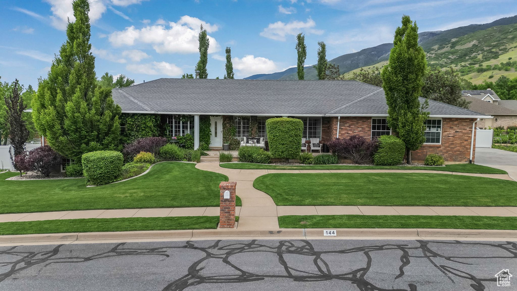 Ranch-style house with a mountain view, a front yard, brick siding, covered porch, and roof with shingles