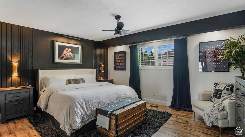 Bedroom with wood finished floors, an accent wall, and a ceiling fan