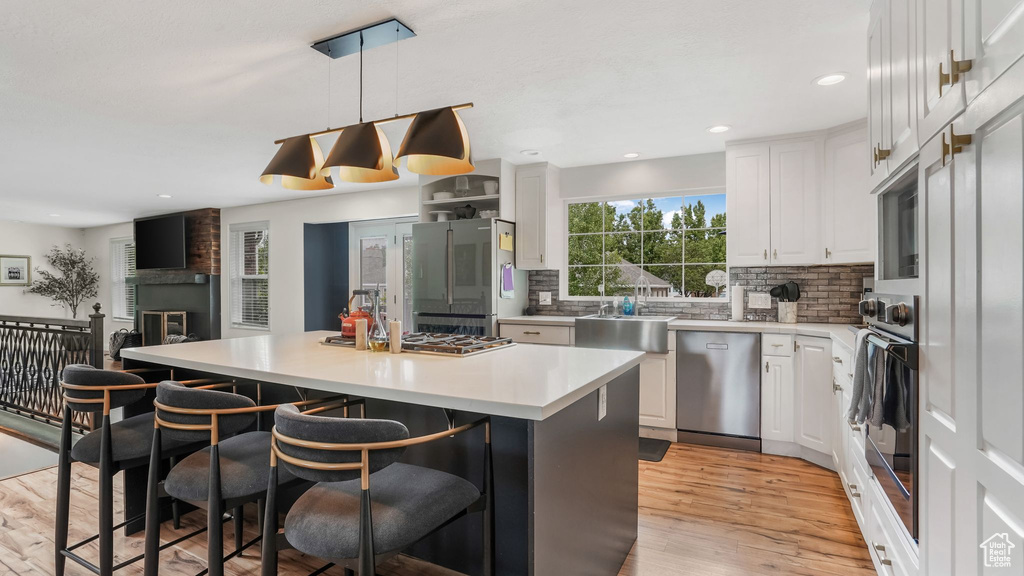 Kitchen featuring black appliances, a breakfast bar area, white cabinets, a center island, and light wood-type flooring