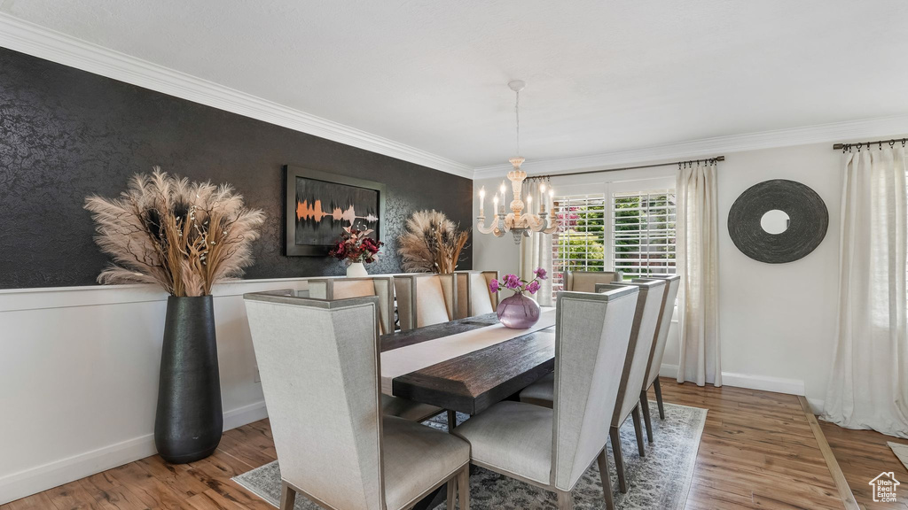 Dining space with a chandelier, wood finished floors, ornamental molding, and an accent wall