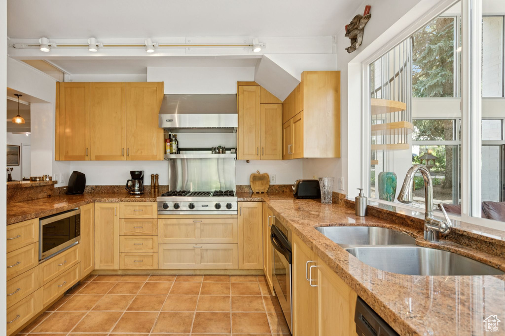 Kitchen featuring stainless steel appliances, ventilation hood, light brown cabinetry, and light tile patterned floors