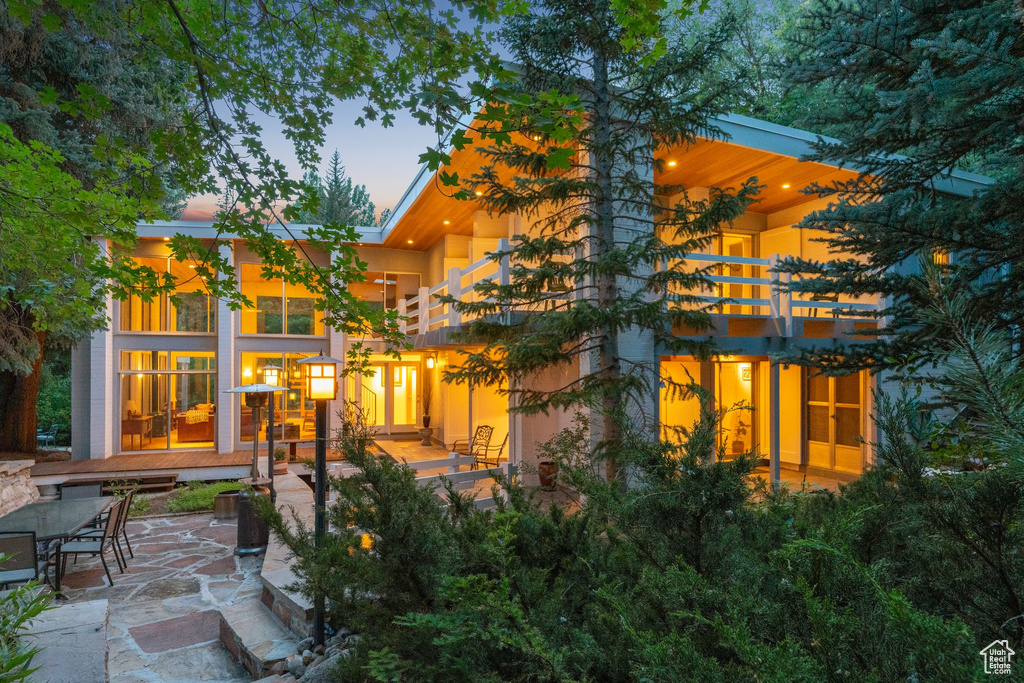 Back of property at dusk with a balcony and a patio