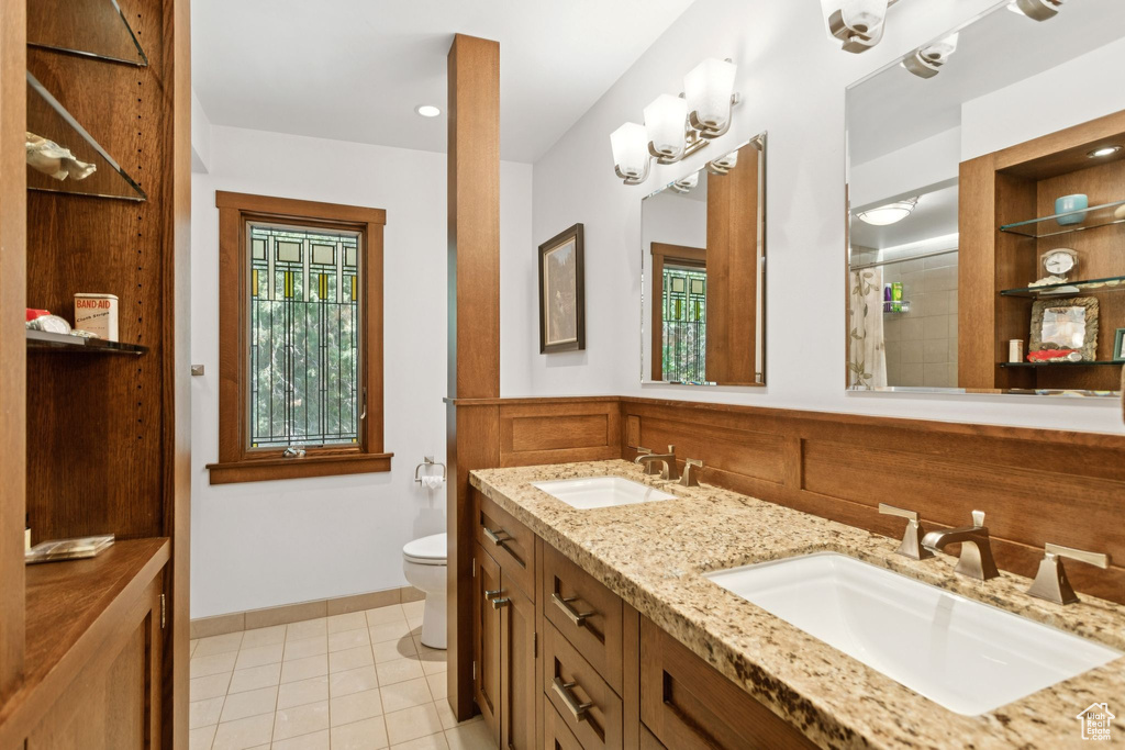 Bathroom featuring double vanity, tile patterned floors, a wainscoted wall, and a shower
