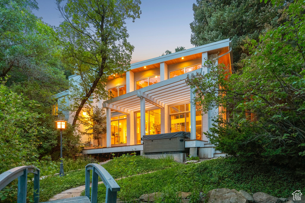 Back of property at dusk with a pergola and a hot tub