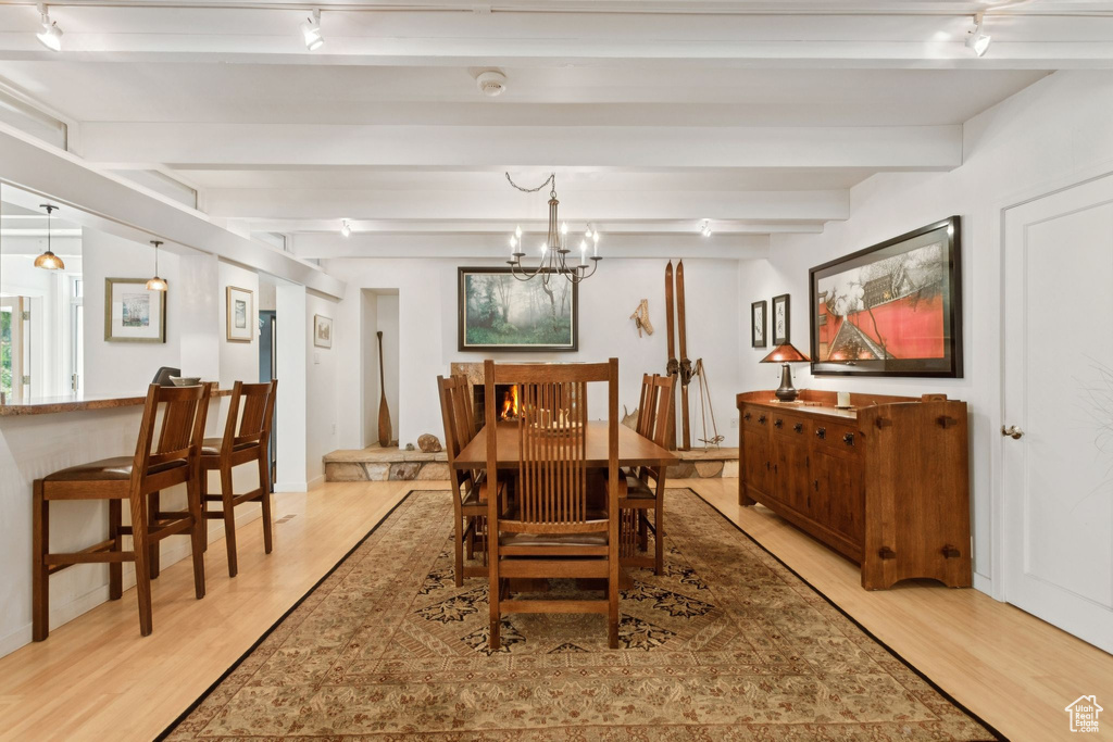 Dining space with rail lighting, light wood-style floors, beam ceiling, and a chandelier