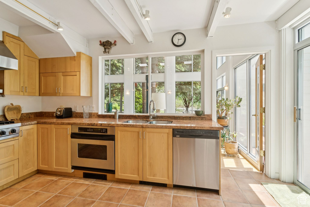 Kitchen featuring appliances with stainless steel finishes, light brown cabinets, beam ceiling, rail lighting, and light tile patterned floors