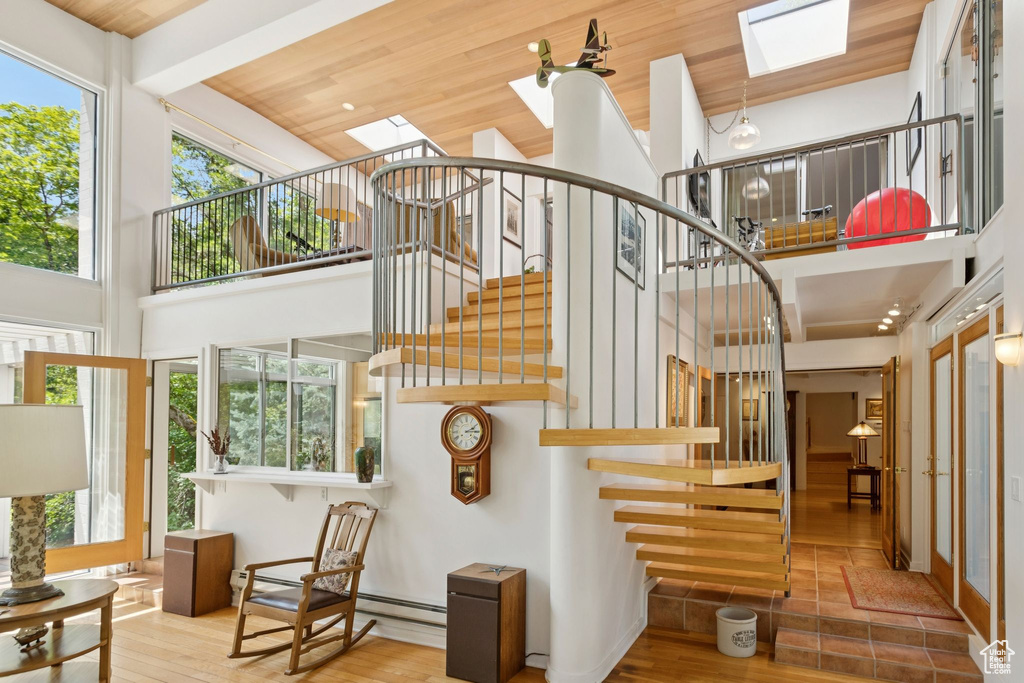 Stairs with a skylight, a towering ceiling, wood ceiling, wood finished floors, and baseboard heating