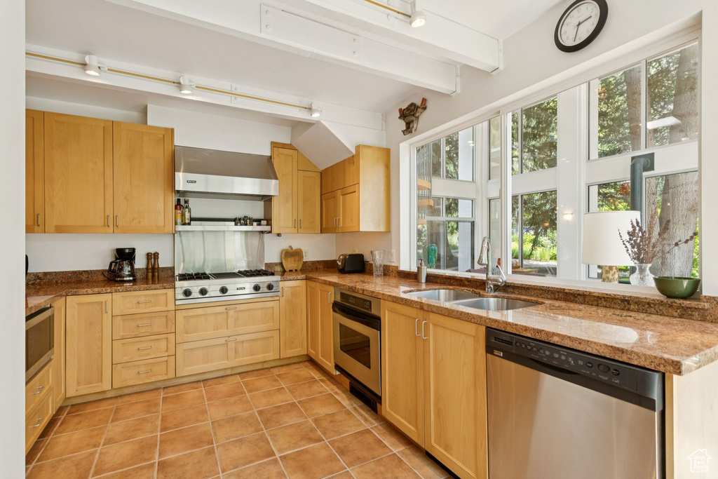 Kitchen featuring stainless steel appliances, light brown cabinets, wall chimney exhaust hood, light tile patterned floors, and stone countertops