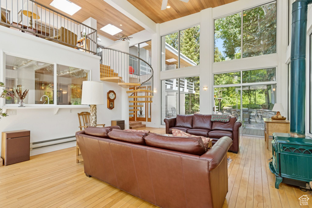 Living room with a towering ceiling, a wood stove, a baseboard heating unit, stairway, and wood-type flooring