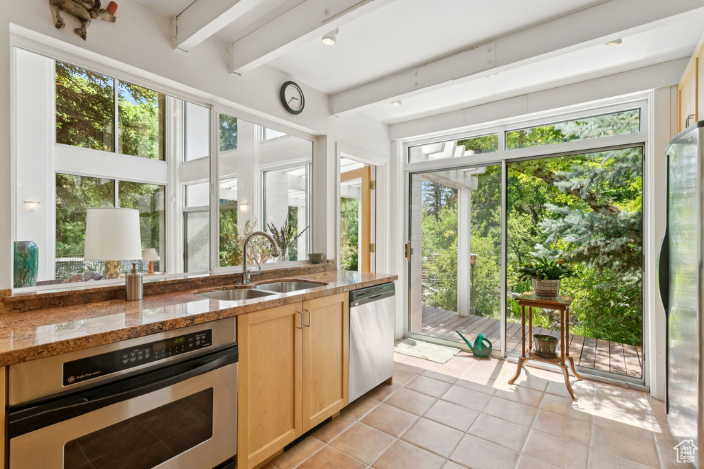 Kitchen with appliances with stainless steel finishes, light brown cabinetry, light tile patterned floors, beam ceiling, and healthy amount of natural light