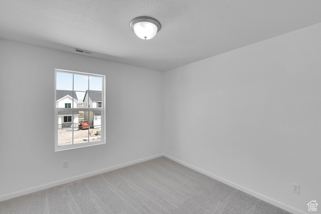 Empty room featuring light colored carpet and a textured ceiling