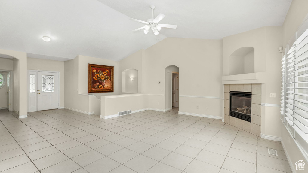 Unfurnished living room featuring a ceiling fan, vaulted ceiling, a tile fireplace, arched walkways, and light tile patterned floors
