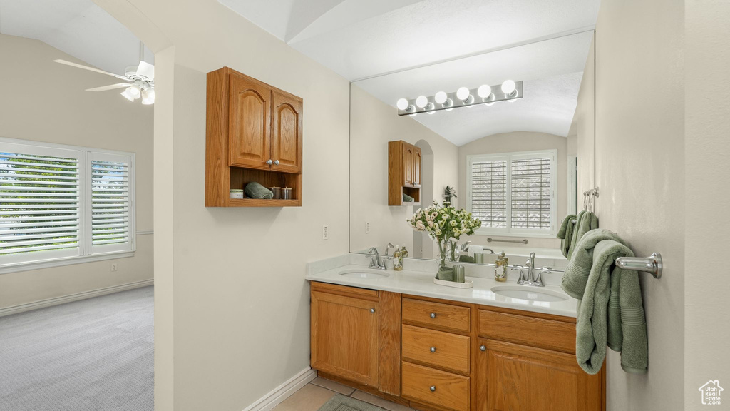 Full bath with lofted ceiling, double vanity, healthy amount of natural light, and ceiling fan