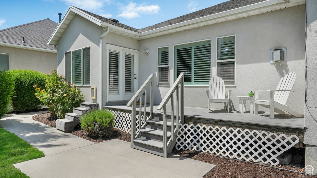 Entrance to property featuring stucco siding, a deck, and roof with shingles