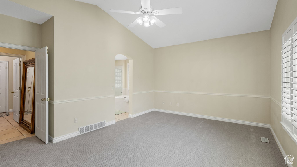 Carpeted empty room featuring ceiling fan, arched walkways, and high vaulted ceiling
