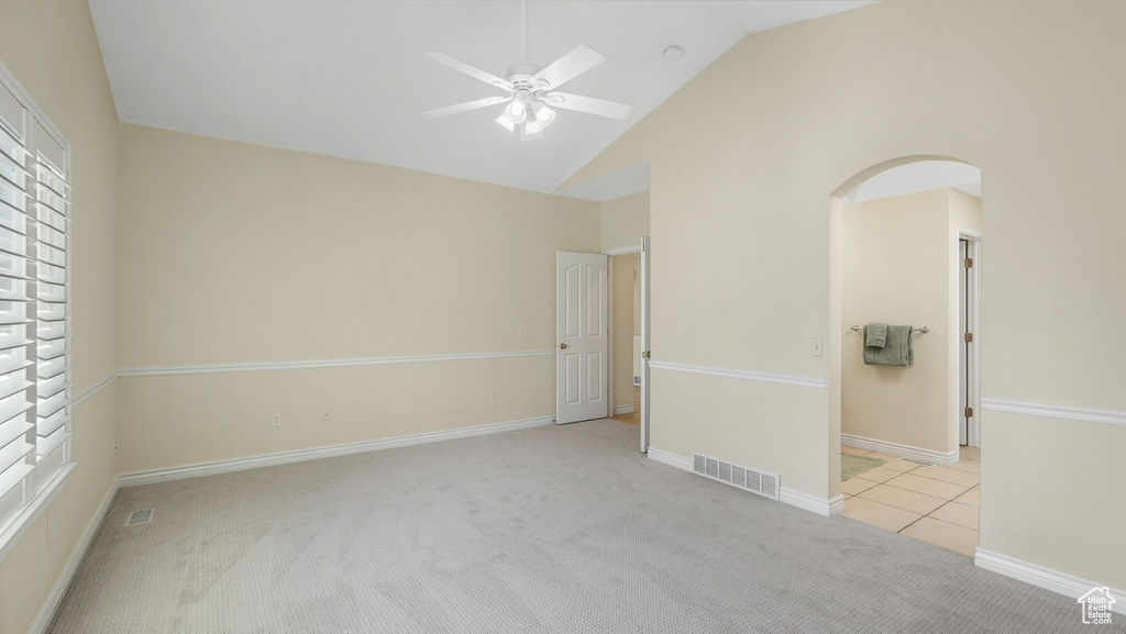 Empty room featuring light colored carpet, ceiling fan, high vaulted ceiling, arched walkways, and plenty of natural light