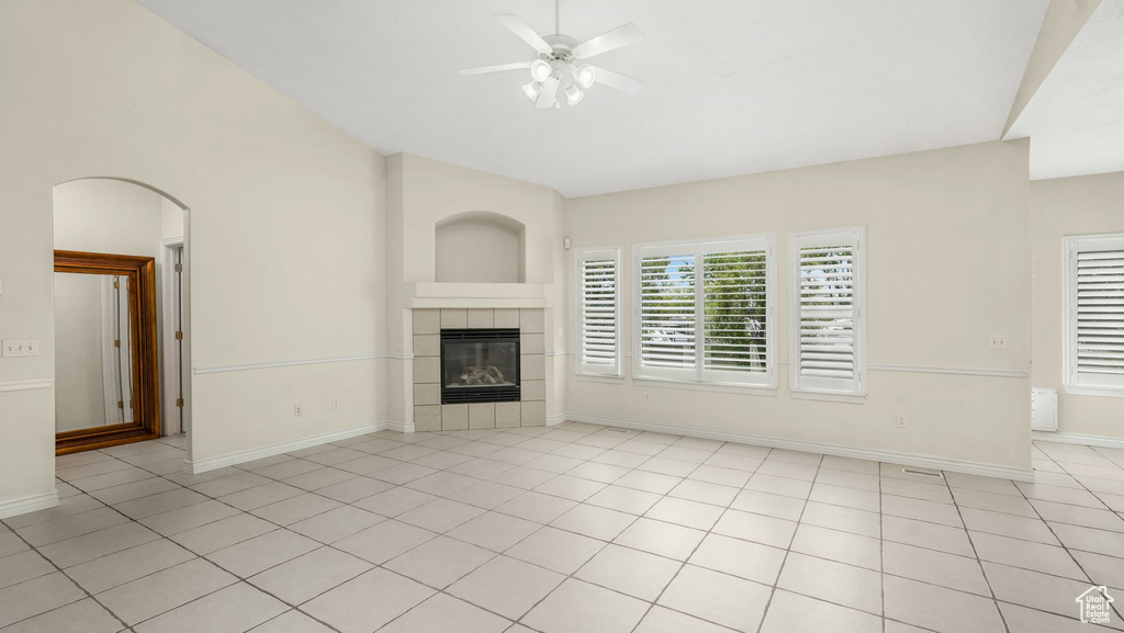 Unfurnished living room featuring ceiling fan, a tile fireplace, light tile patterned floors, and arched walkways