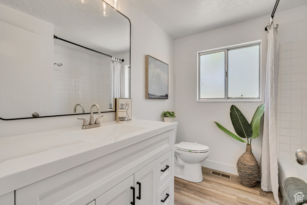Bathroom featuring vanity, wood finished floors, a textured ceiling, and shower / bathtub combination with curtain