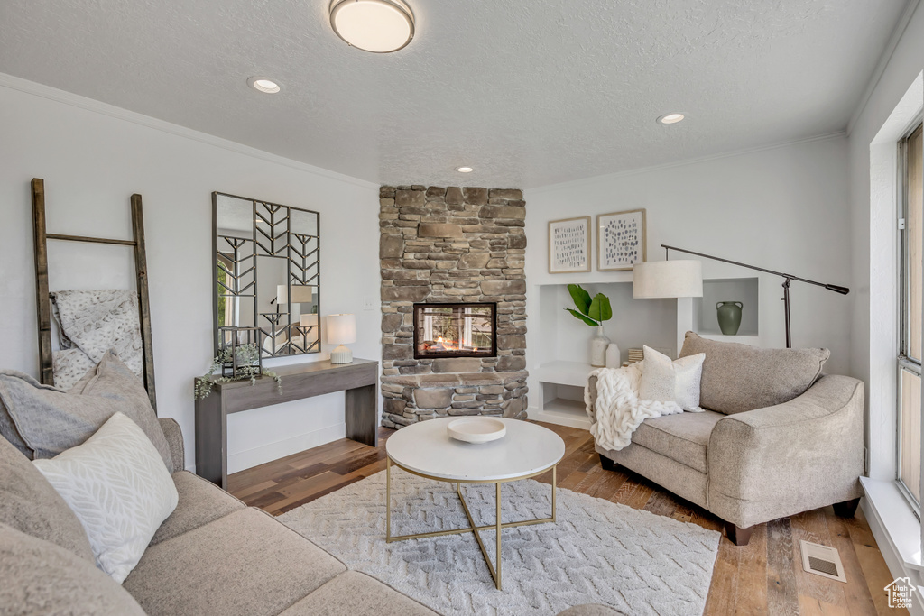 Living area with wood finished floors, a fireplace, a textured ceiling, recessed lighting, and crown molding