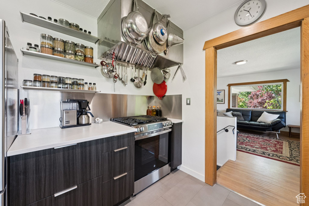 Kitchen with stainless steel range with gas cooktop, open shelves, extractor fan, and light tile patterned floors