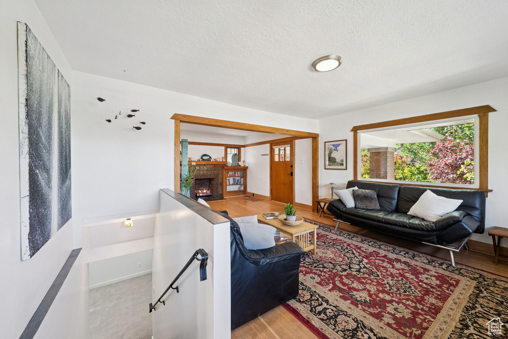 Living area with a brick fireplace, a textured ceiling, and light wood finished floors
