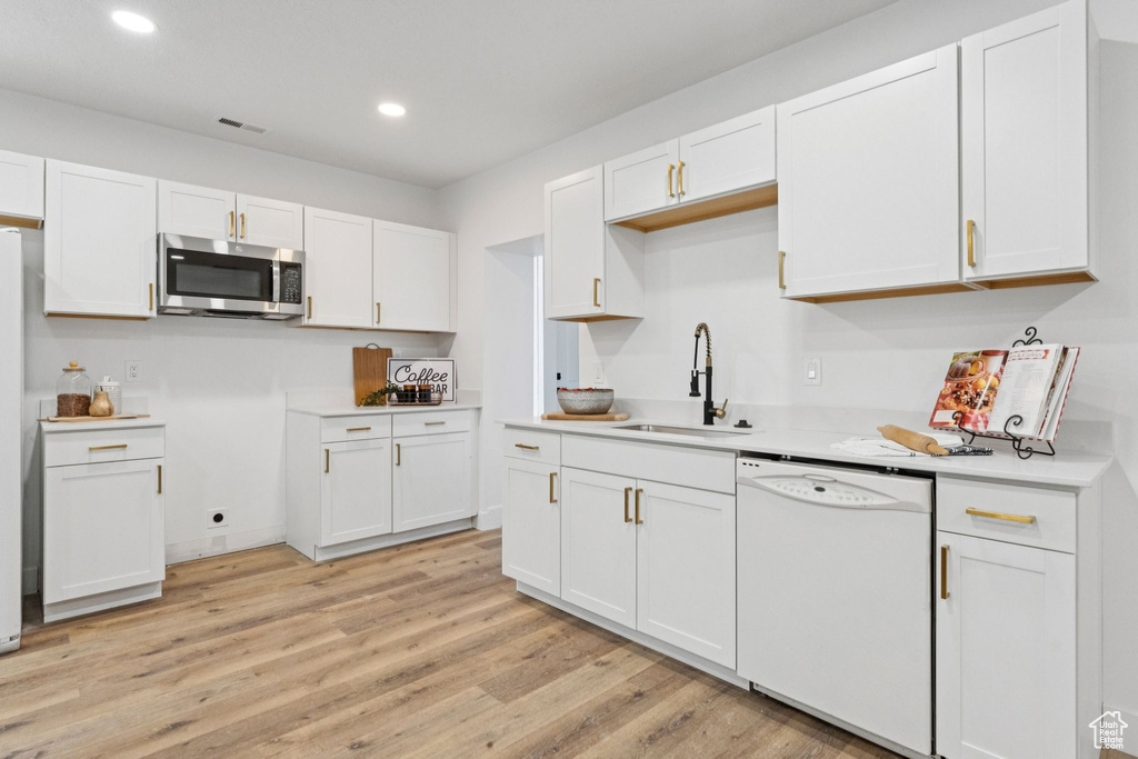 Kitchen featuring stainless steel microwave, dishwasher, light wood finished floors, recessed lighting, and white cabinetry