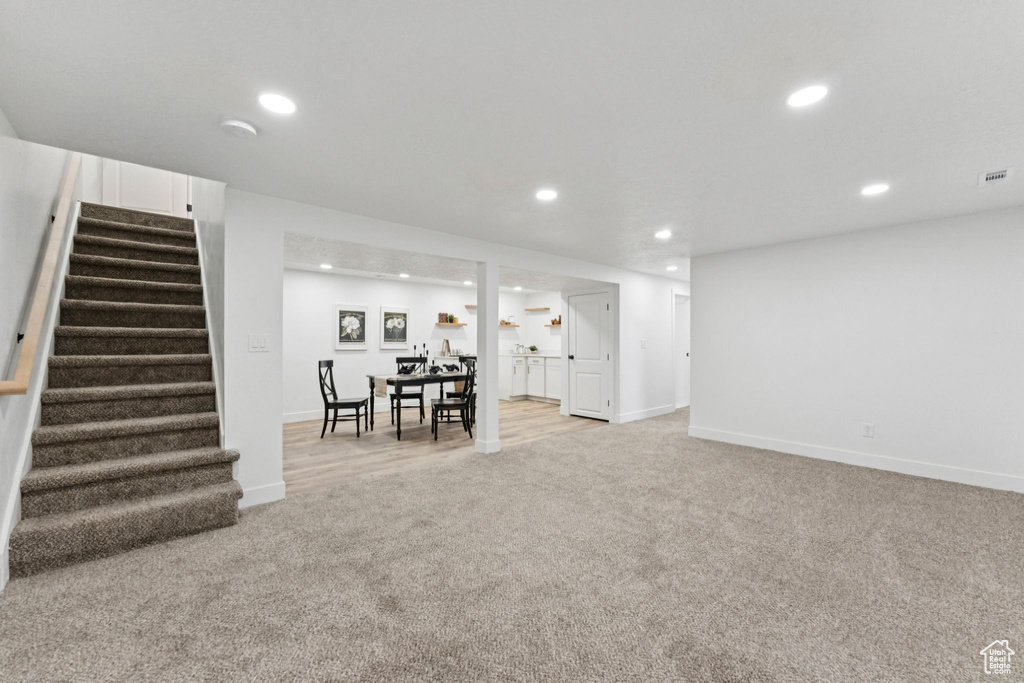 Finished below grade area with light colored carpet, stairs, and recessed lighting