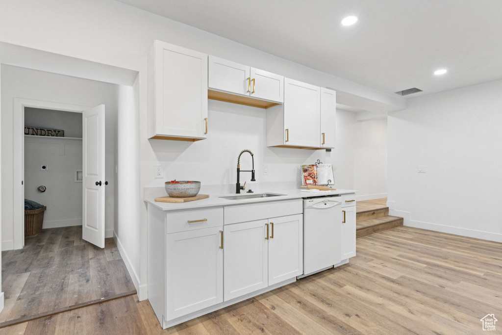 Kitchen with white dishwasher, light countertops, white cabinets, light wood-style flooring, and recessed lighting