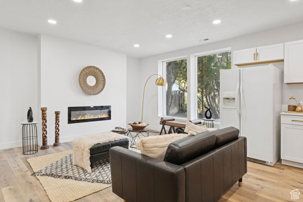 Living room featuring recessed lighting, a glass covered fireplace, and light wood finished floors