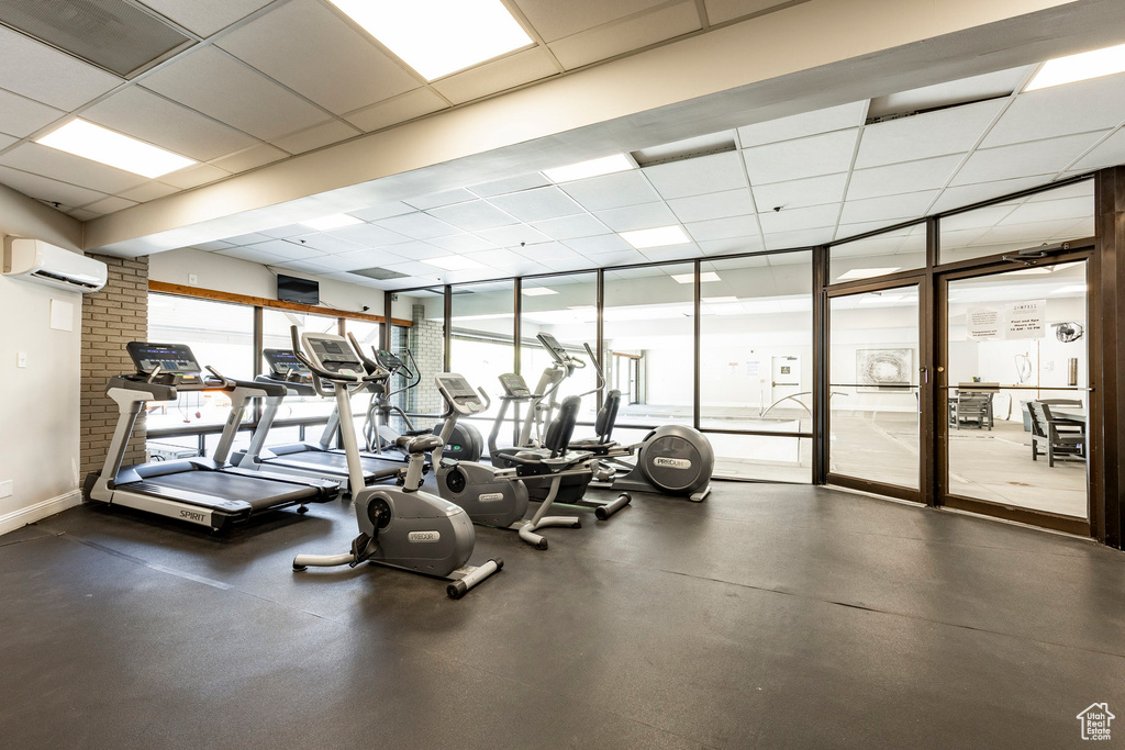 Workout area featuring a wall mounted air conditioner, a paneled ceiling, and a wall of windows