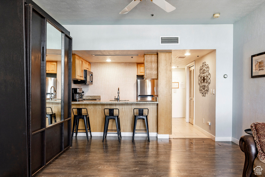 Kitchen featuring freestanding refrigerator, black microwave, wood finished floors, a breakfast bar area, and a ceiling fan
