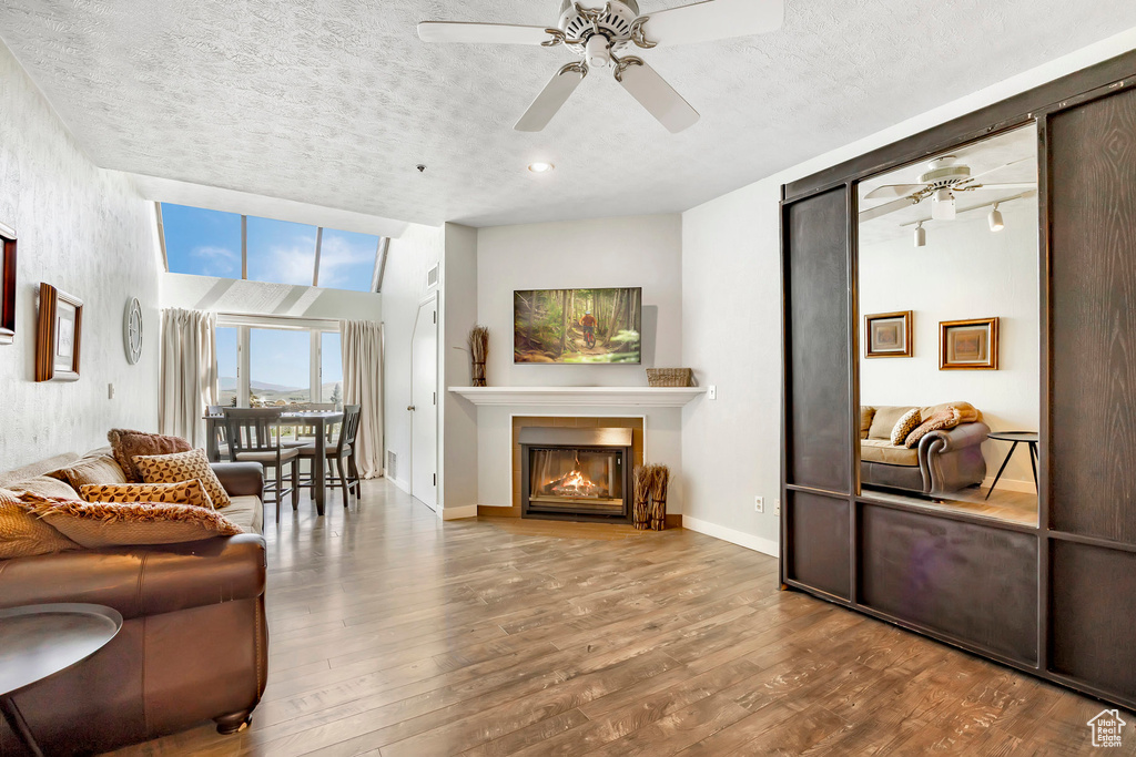 Living room featuring ceiling fan, wood finished floors, a textured ceiling, and a glass covered fireplace